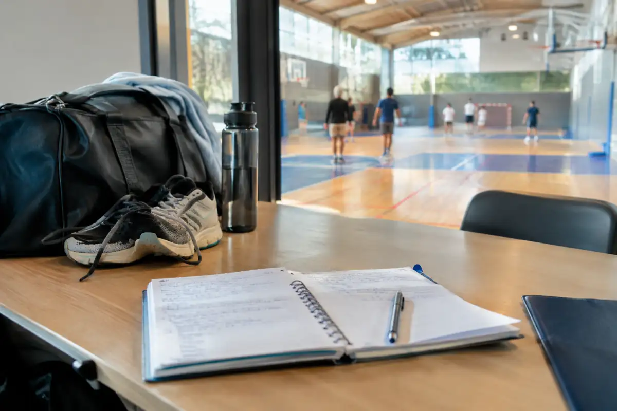 Cahier de cours et sac de sport près d’un gymnase, symbole de l’équilibre entre scolarité et entraînement.
