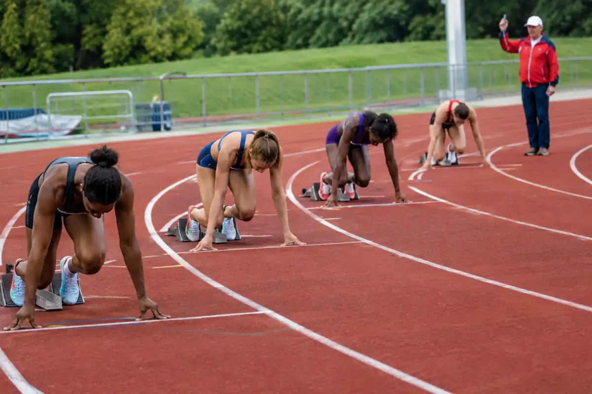 Départ d’un 400 mètres en couloirs décalés : les coureurs sont en starting-blocks sous le contrôle du starter.