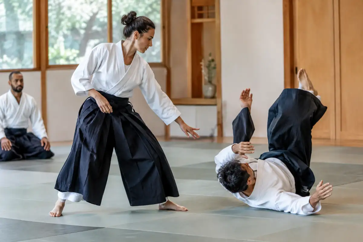 Deux pratiquants d’aïkido en keikogi travaillent une projection et une chute contrôlée sur le tatami.