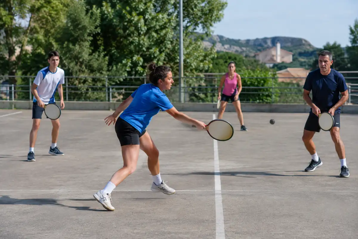 Balle au tambourin : des joueurs renvoient une balle avec leur tambourin rond sur un terrain extérieur tracé au sol.
