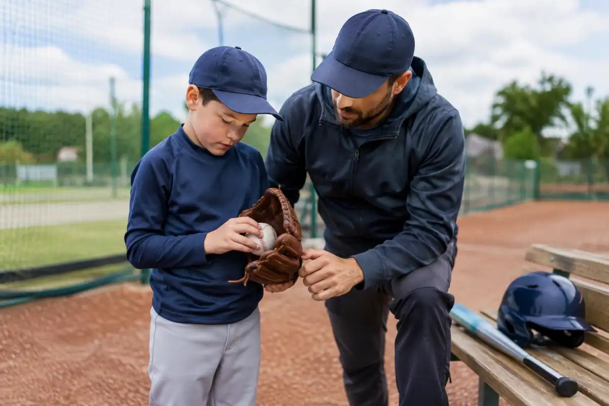Un débutant essaie un gant de baseball sous le regard d’un entraîneur, avec une batte et un casque posés à proximité.
