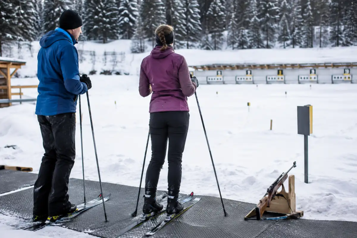 Débutant en ski nordique qui récupère au pas de tir avant une séance de biathlon encadrée par un entraîneur.