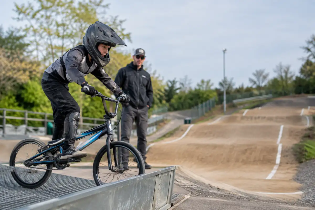Un débutant en BMX race répète un départ sur la grille, sous le regard d’un entraîneur placé hors de la trajectoire.