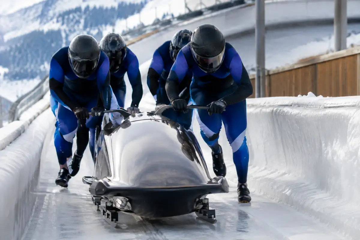 Équipage de bobsleigh en combinaison et casque poussant son engin sur la piste glacée de La Plagne avant le départ.