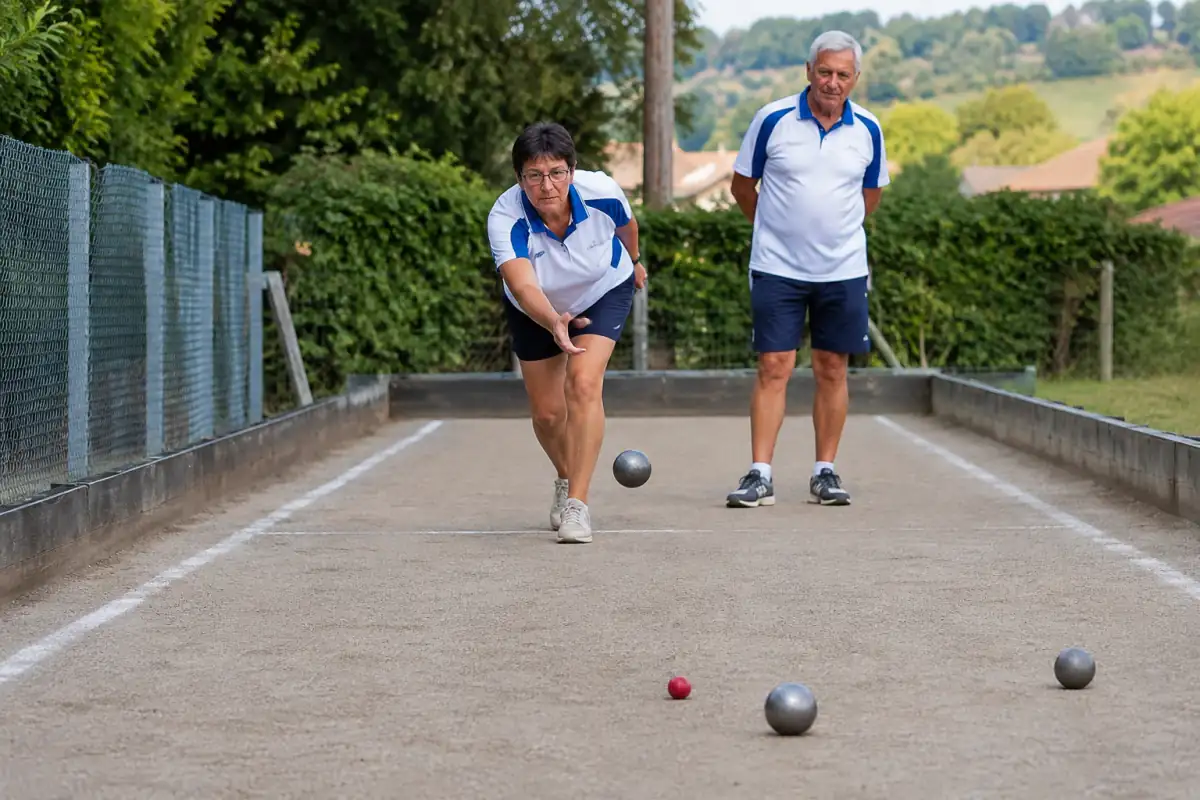 Un joueur lance une boule métallique vers le but sur un terrain balisé lors d’une partie de bocce volo en club.