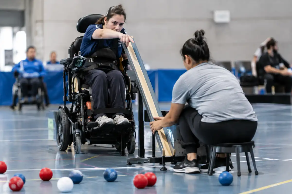 Un joueur BC3 indique l’orientation de sa rampe tandis que son assistant l’ajuste sur un terrain de boccia.
