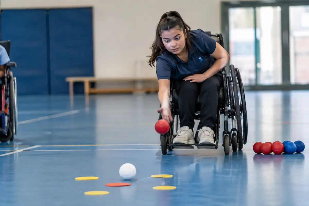 Un joueur de boccia en fauteuil vise le jack pendant un exercice de précision avec des repères au sol et plusieurs boules.