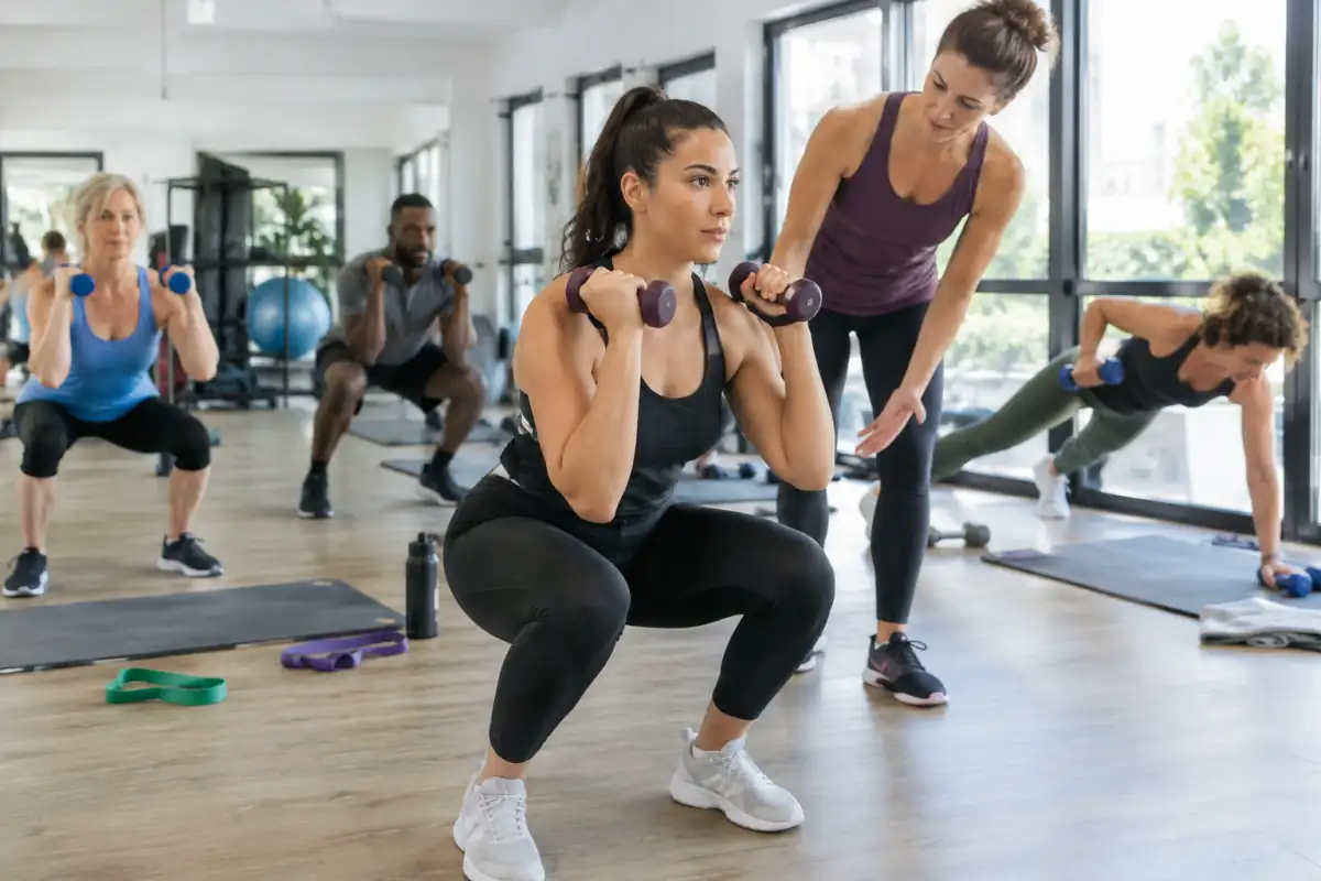 Cours de Body Sculpt en salle : une participante réalise un squat avec des haltères légers sous le regard du coach.