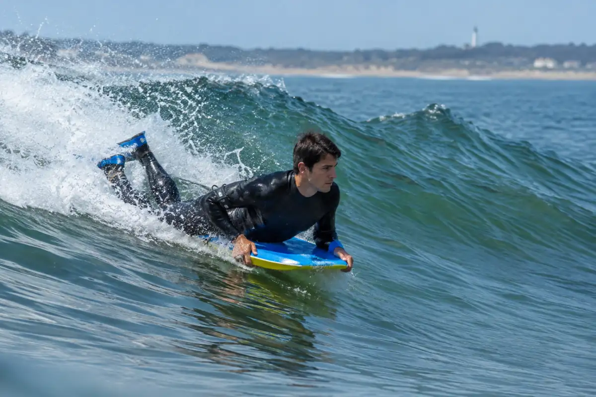 Un pratiquant de bodyboard allongé sur sa planche suit une vague de l’Atlantique, palmes aux pieds et combinaison portée.