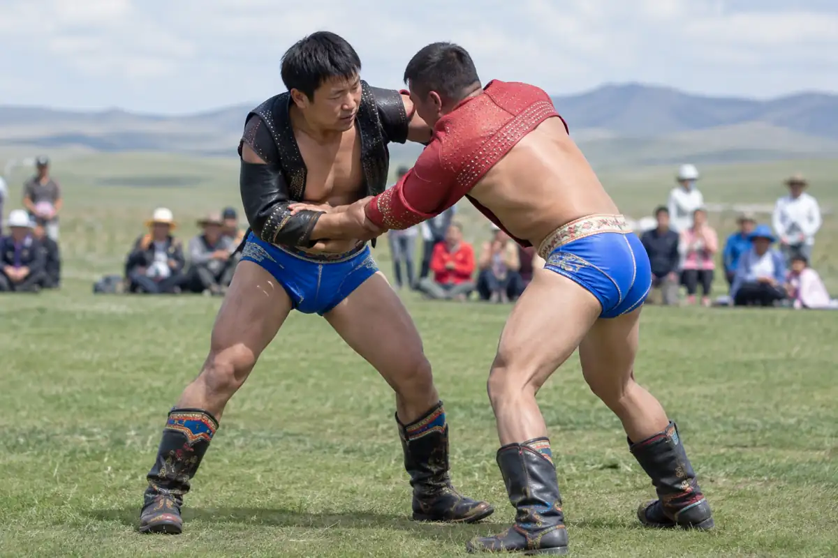 Deux lutteurs en tenue traditionnelle mongole s’affrontent debout sur l’herbe lors d’un combat de bökh.