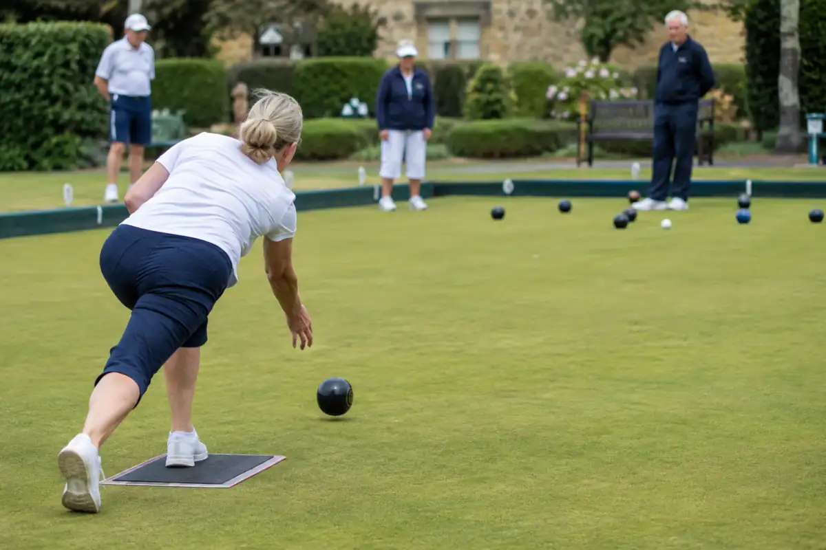 Un joueur lance une boule anglaise sur un green tandis que les bowls s’approchent du jack blanc dans le rink.