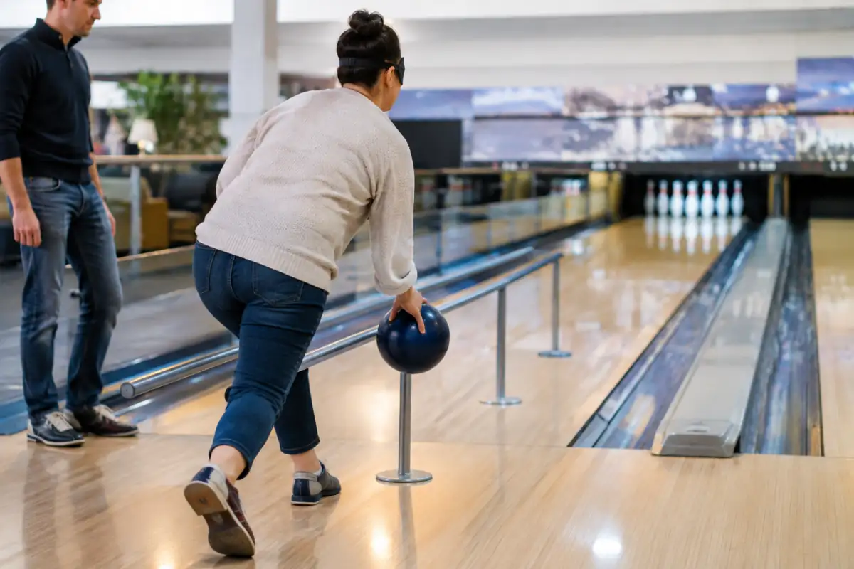 Joueur déficient visuel aligné sur une piste de bowling à l’aide d’un guide tactile avant de lancer sa boule vers les quilles.