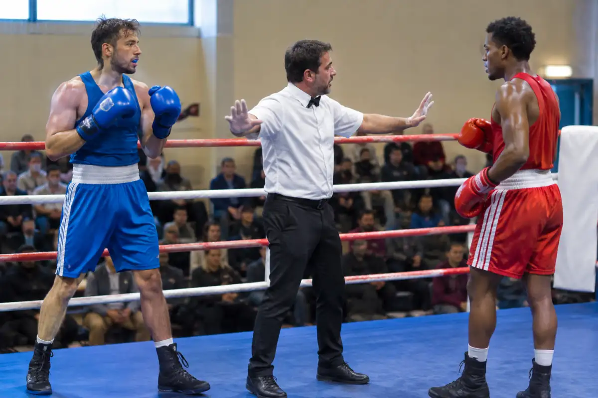 Un arbitre sépare deux boxeurs dans le ring après avoir interrompu l’échange pour faire respecter les règles.