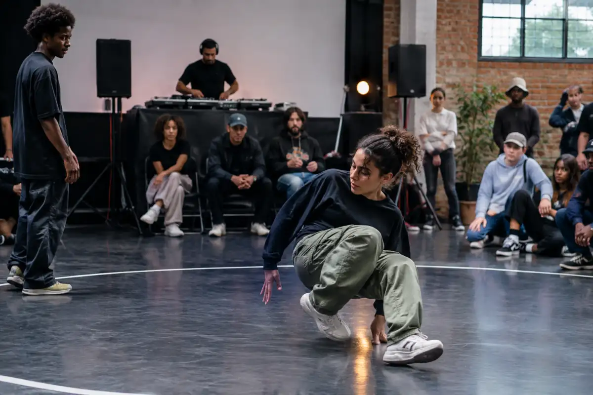 Un danseur improvise dans le cercle d’une battle de breaking tandis que son adversaire attend son tour et que le jury observe.