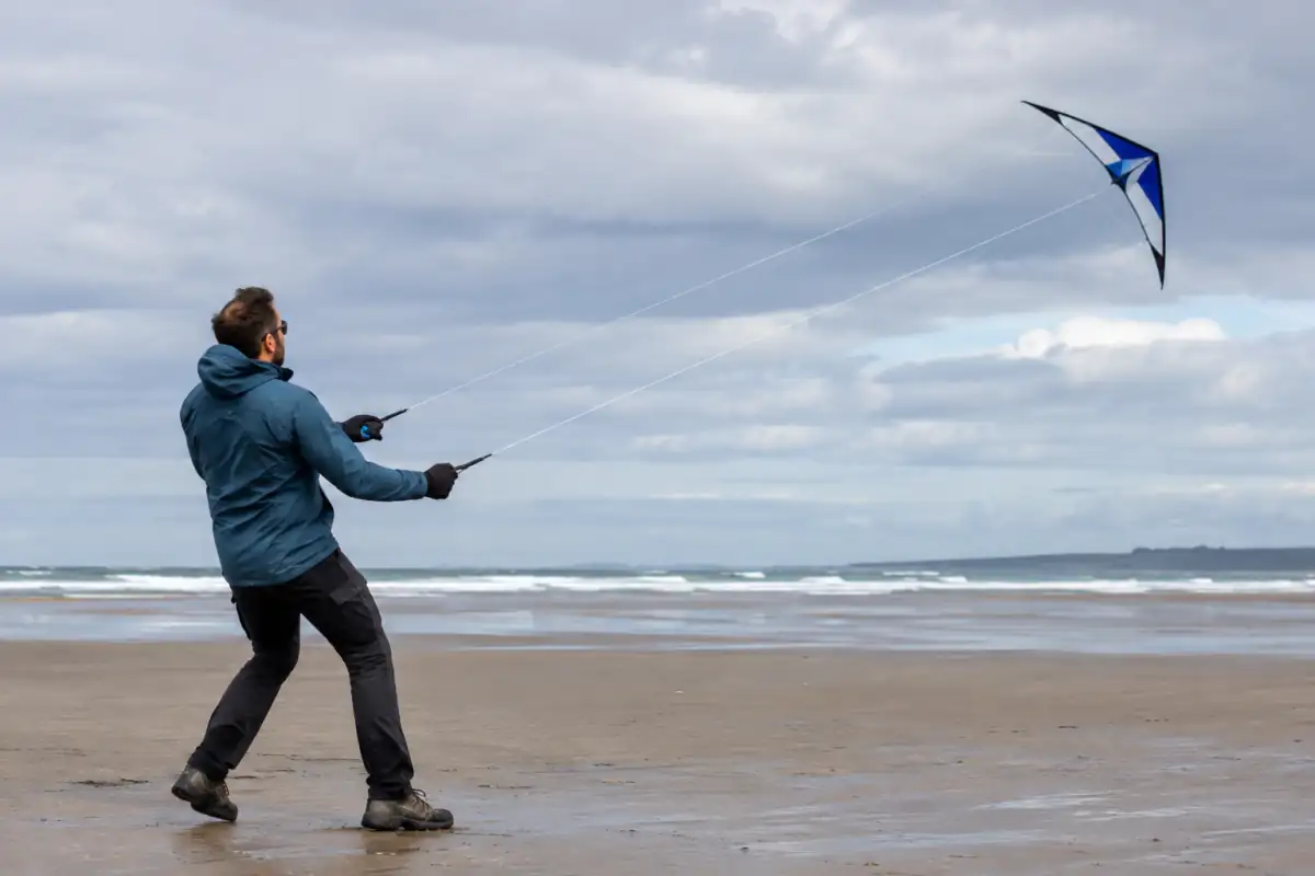 Pilote de cerf-volant acrobatique dirigeant un modèle à deux lignes lors d’un vol sur une plage dégagée.