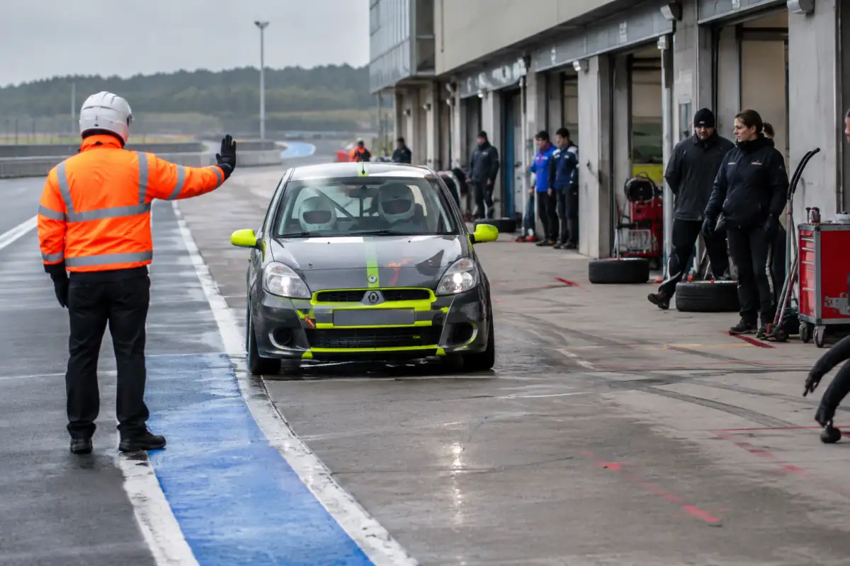 Un instructeur guide un pilote débutant en voiture d’endurance lors d’une séance encadrée dans la voie des stands.