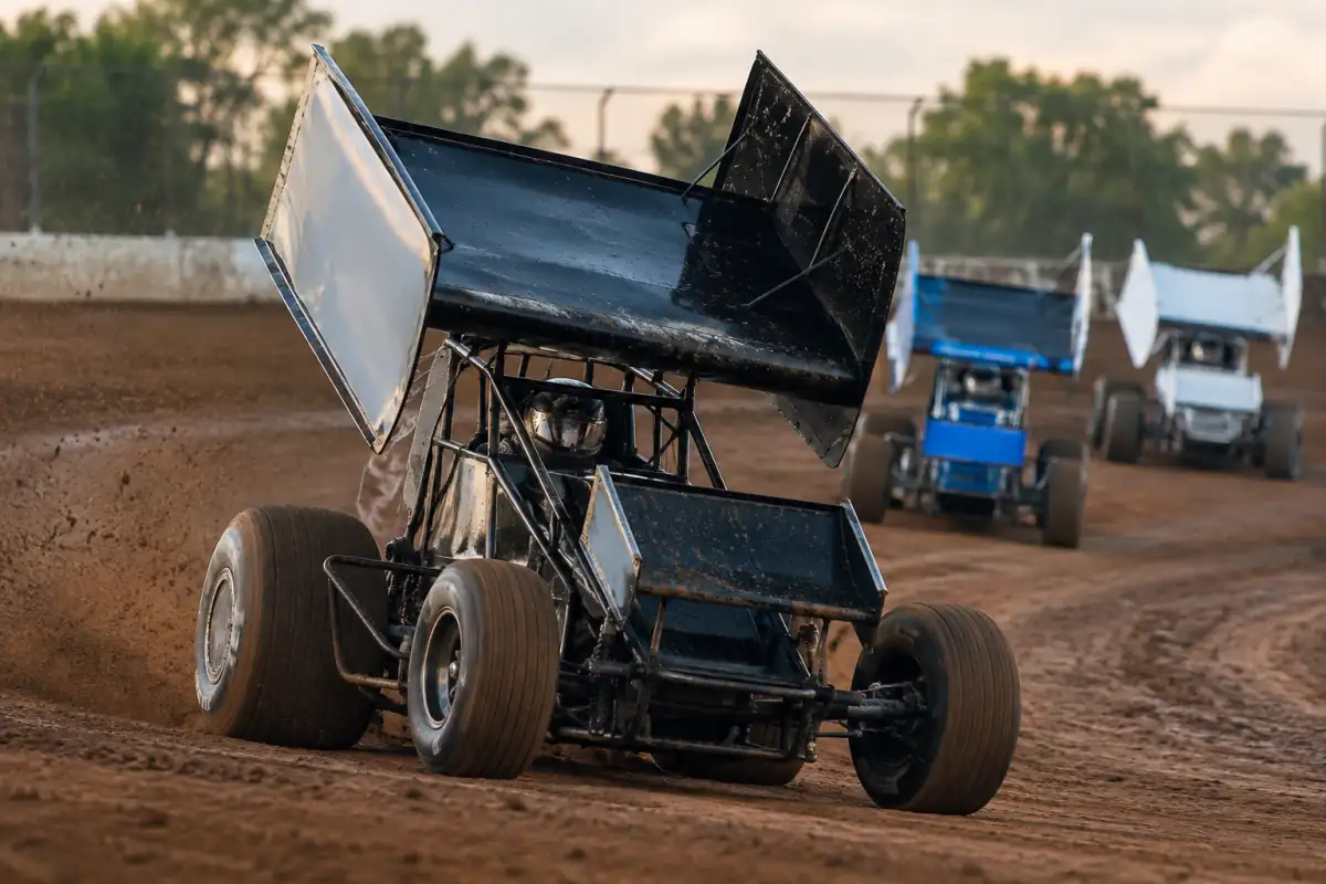 Sprint car à roues découvertes en glisse contrôlée dans un virage d’un circuit ovale en terre battue.