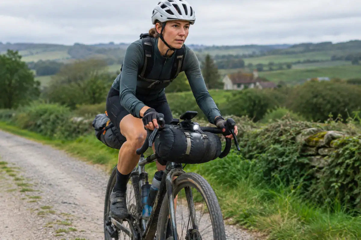 Cycliste en course de bikepacking sur une piste rurale française, avec sacoches de cadre, de selle et de guidon.