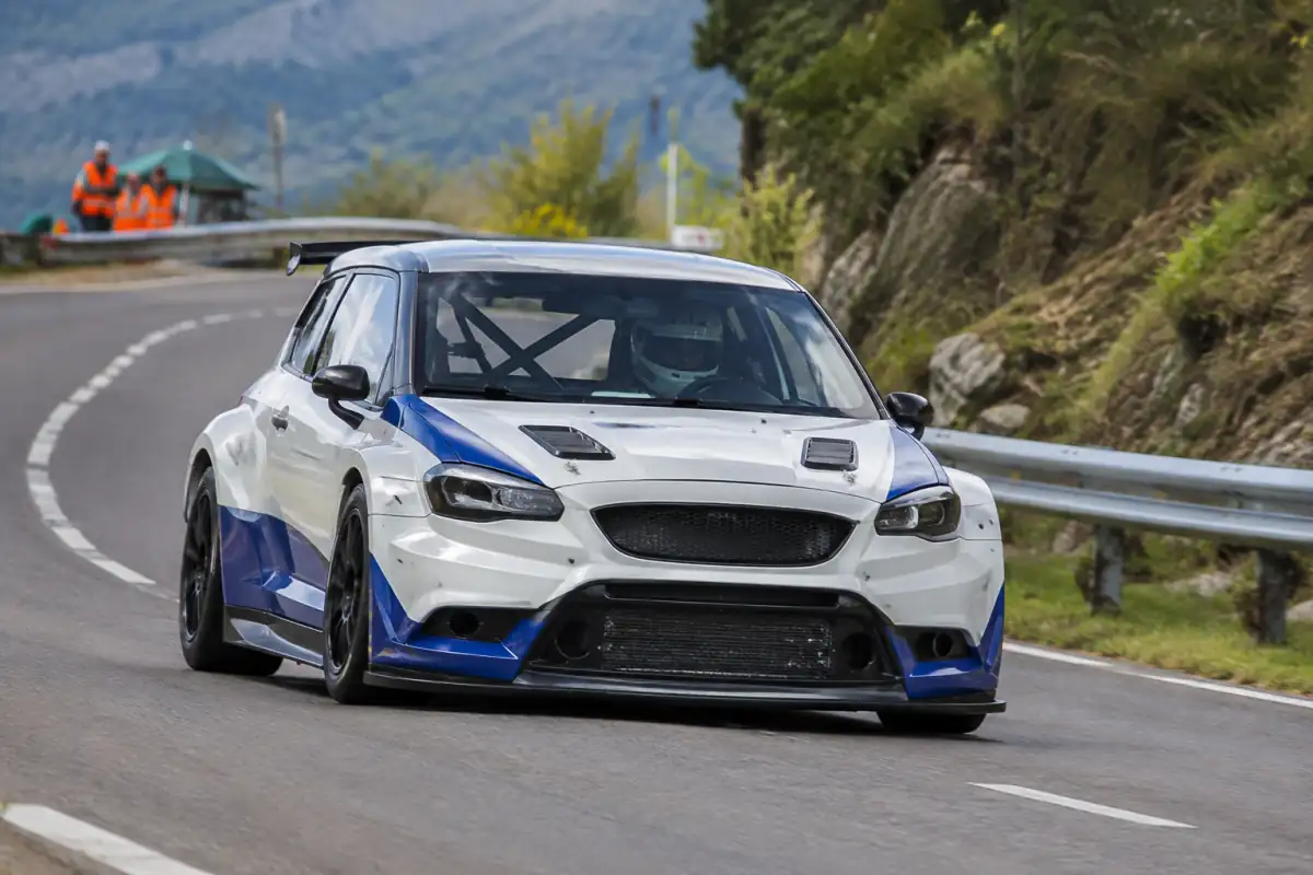 Une voiture de compétition pilotée par un conducteur casqué grimpe un virage fermé lors d’une course de côte automobile.