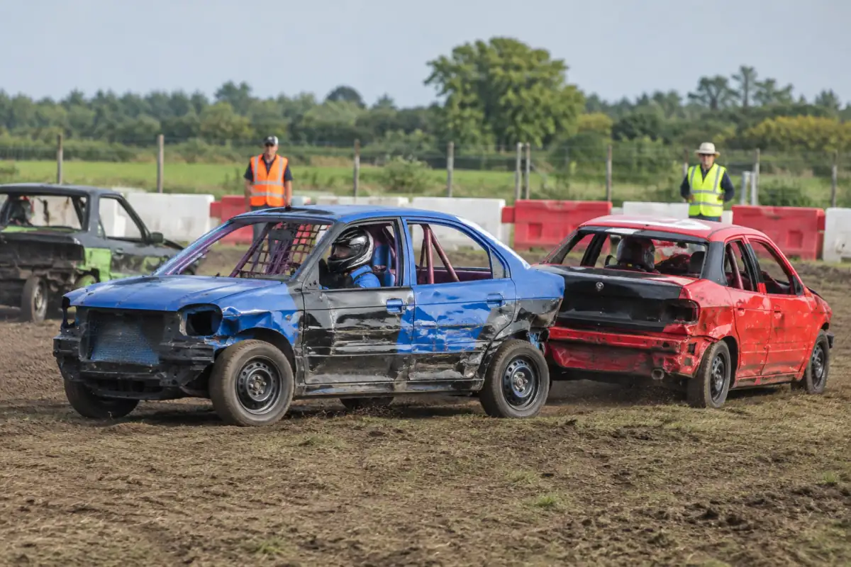 Course de démolition automobile dans une arène fermée, avec voitures préparées, pilote casqué et barrières de sécurité.