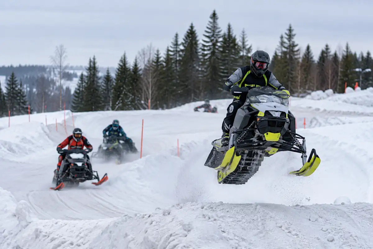 Course de snocross sur un circuit enneigé : un pilote en motoneige franchit une bosse devant d’autres concurrents.