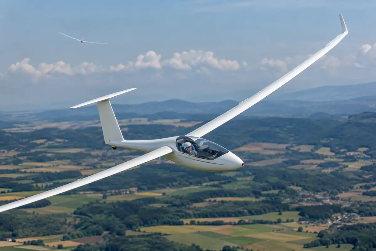 Planeur de compétition en virage au-dessus de la campagne française, son pilote exploite une ascendance pour poursuivre le parcours.