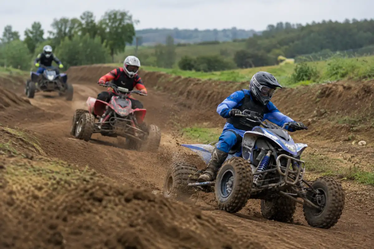 Des pilotes en tenue de protection négocient un virage de terre pendant une course de quad cross sur circuit.