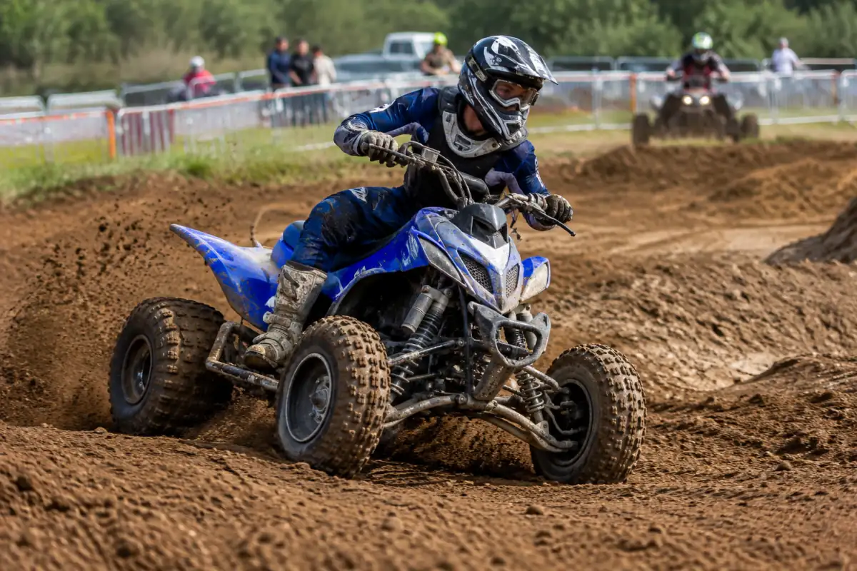 Pilote équipé prenant un virage sur son quad pendant une course de quad cross sur un circuit tout-terrain.