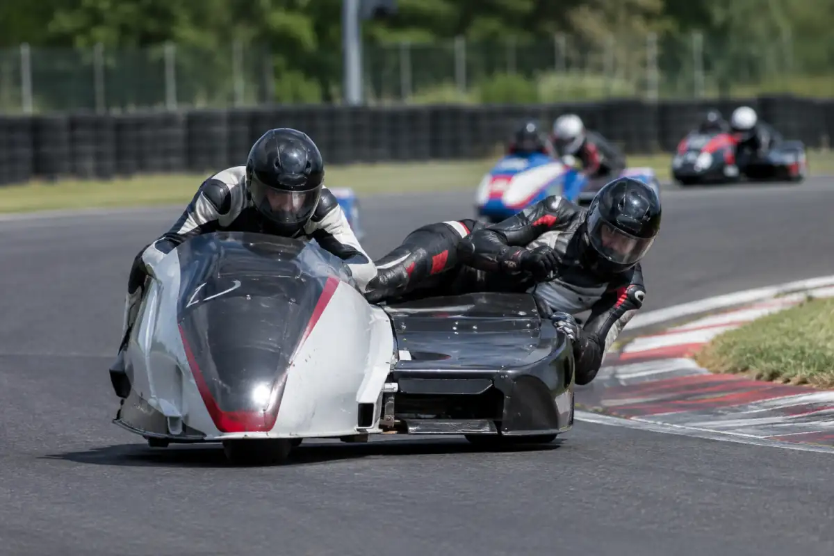 Équipage de course de side-car en virage sur circuit, avec le pilote au guidon et le passager déporté sur la plateforme.