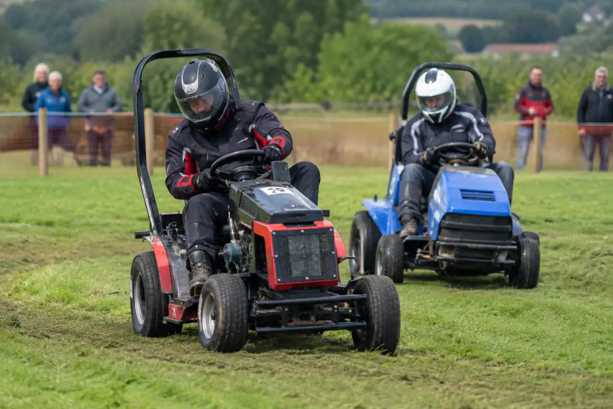 Pilotes en casque intégral négociant un virage sur des tondeuses de course préparées, sur un circuit fermé en herbe.