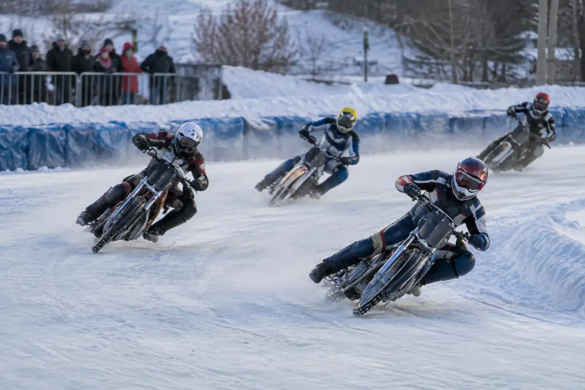 Pilotes en pleine course de vitesse moto sur glace, penchés dans un virage sur un ovale gelé avec leurs motos à pneus cloutés.