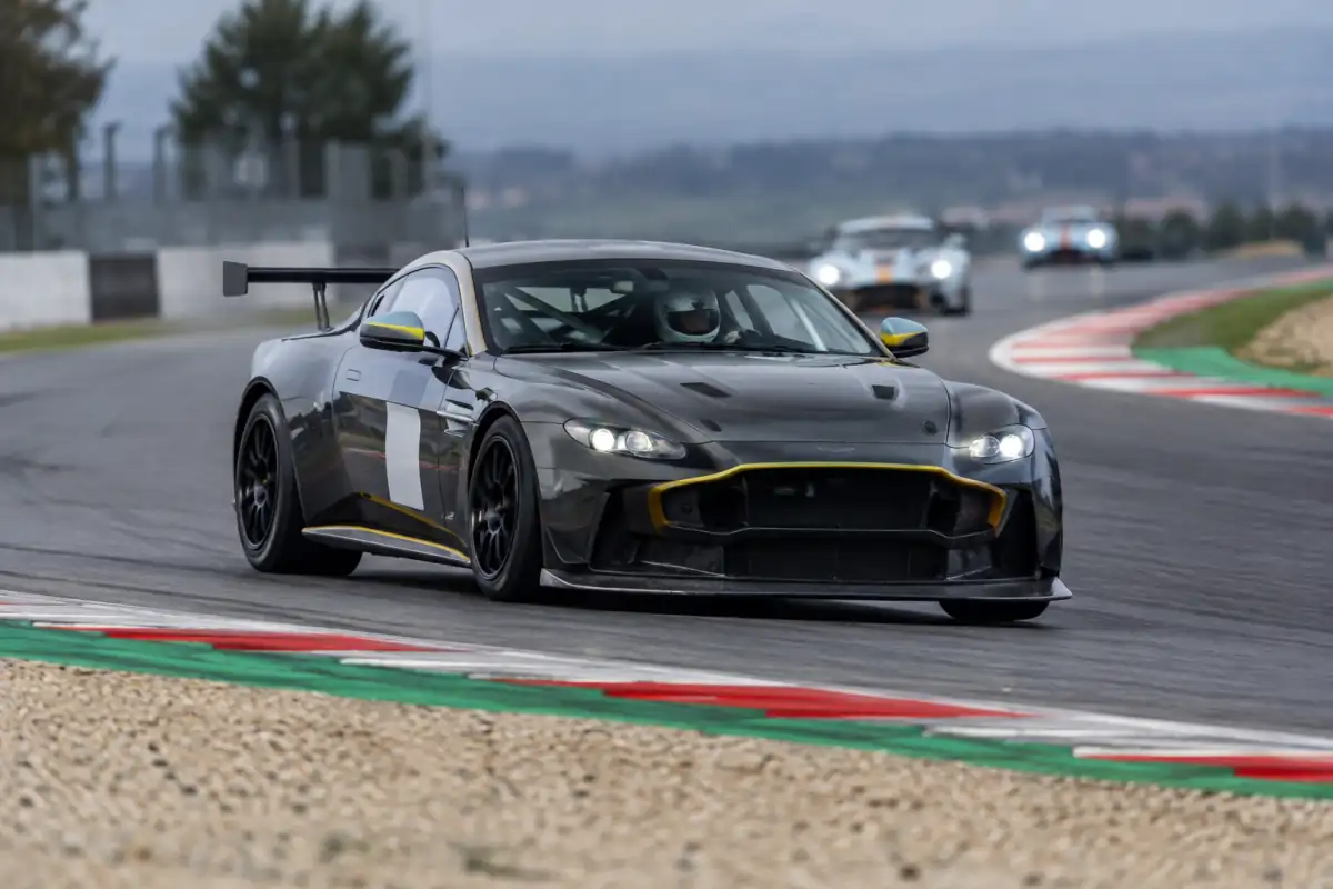 Une voiture GT4 négocie un virage sur circuit, avec ses pneus de course, son aileron et ses équipements de sécurité.