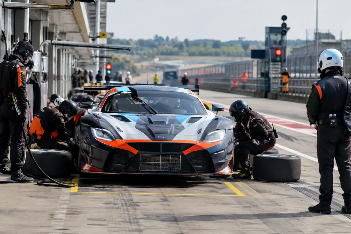 Une voiture GT immobilisée dans son emplacement pendant un changement de pneus encadré par l’équipe, dans la voie des stands.