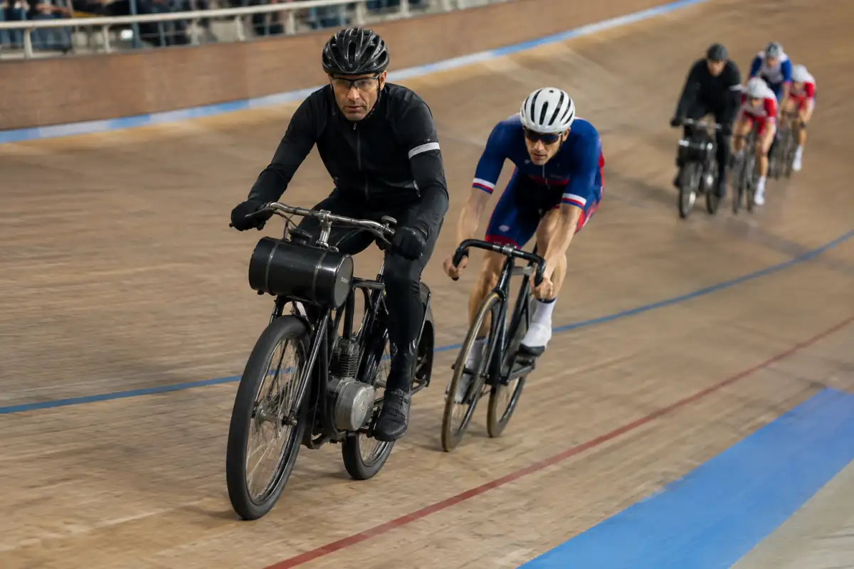 Course derrière derny sur un vélodrome : des cyclistes en tenue de piste suivent de près un pilote motorisé dans le virage.