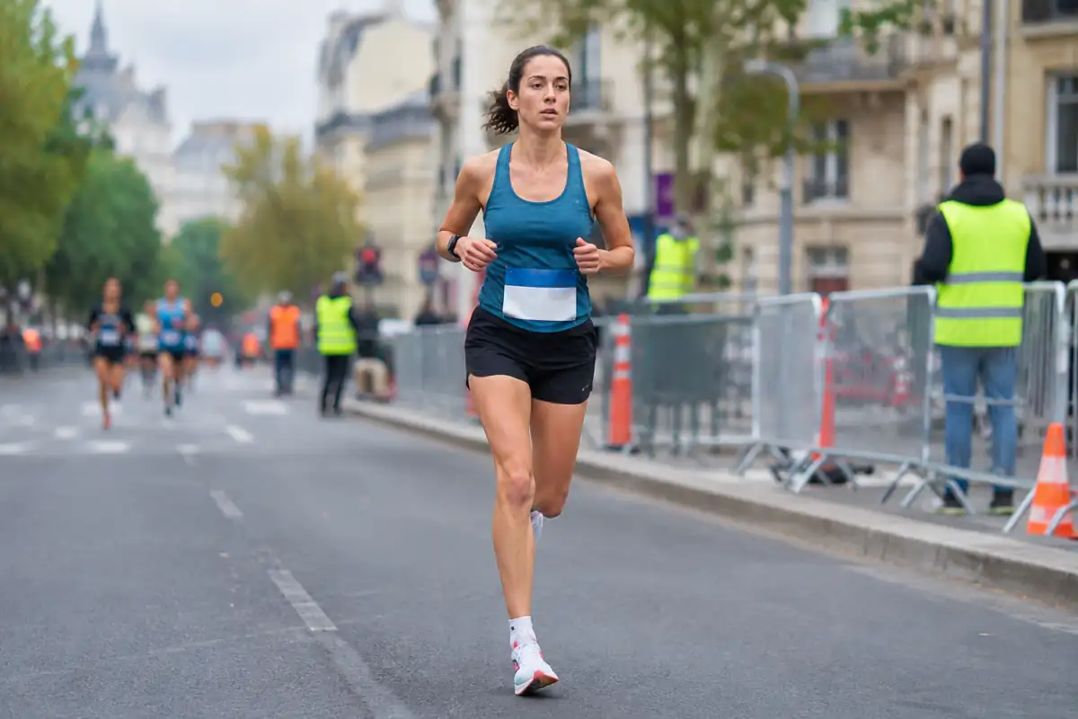 Une coureuse en tenue technique avance sur une route goudronnée balisée lors d’une course sur route en ville.