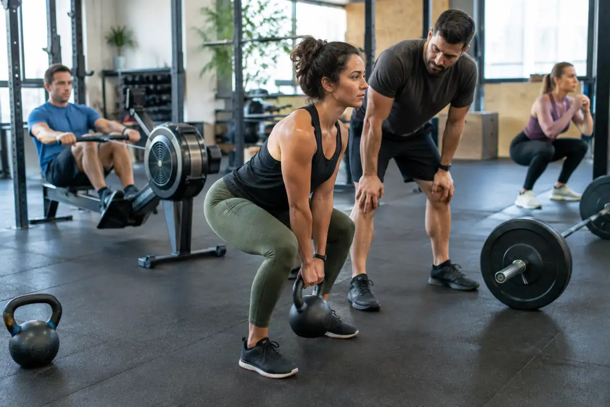 Séance de cross-training en salle : une pratiquante réalise un soulevé de kettlebell sous l’œil d’un coach.