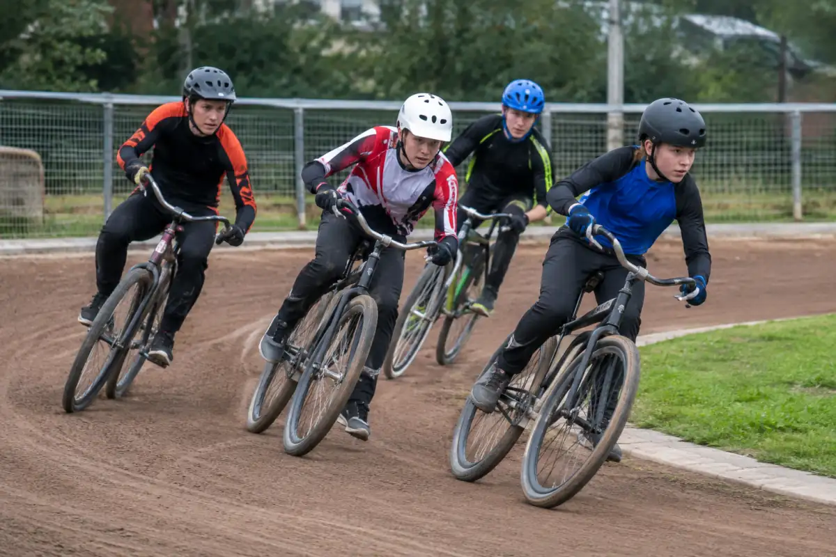 Quatre coureurs disputent une manche de cycle speedway sur une piste ovale en terre, au coude à coude dans un virage serré.