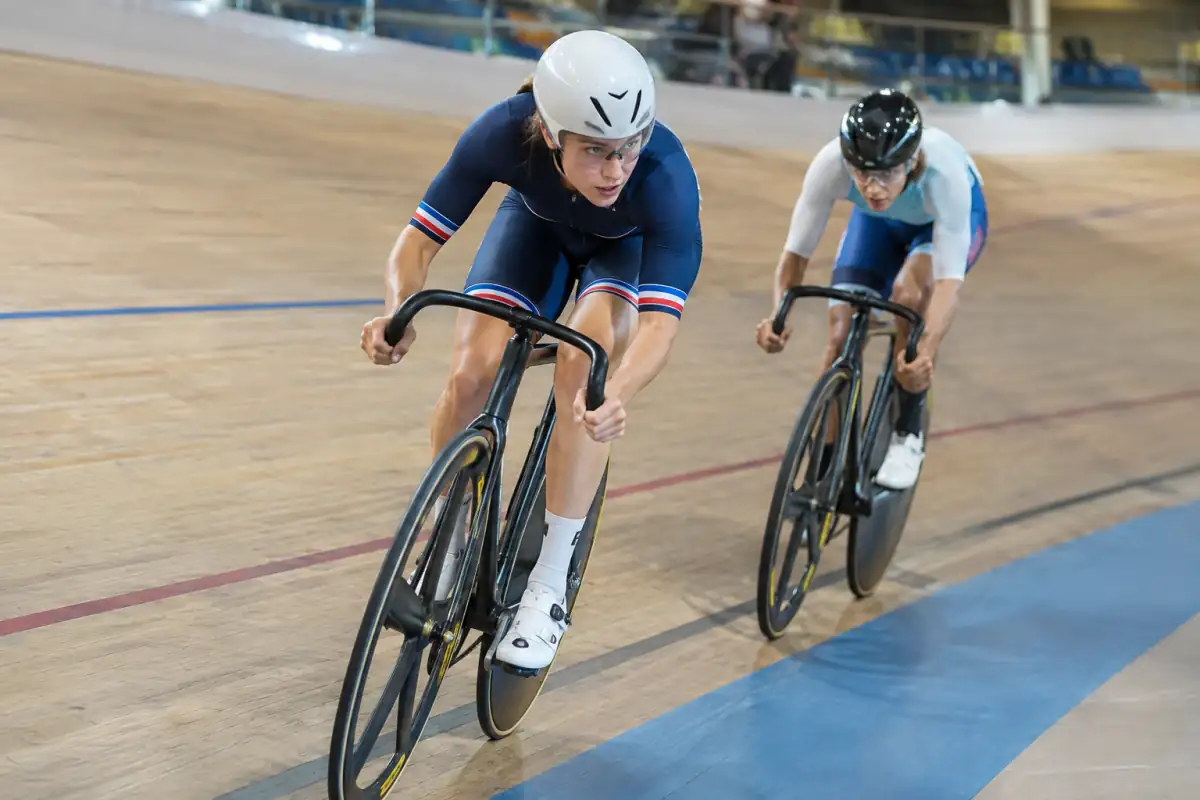 Deux cyclistes en action sur leurs vélos à pignon fixe dans un virage incliné de vélodrome.