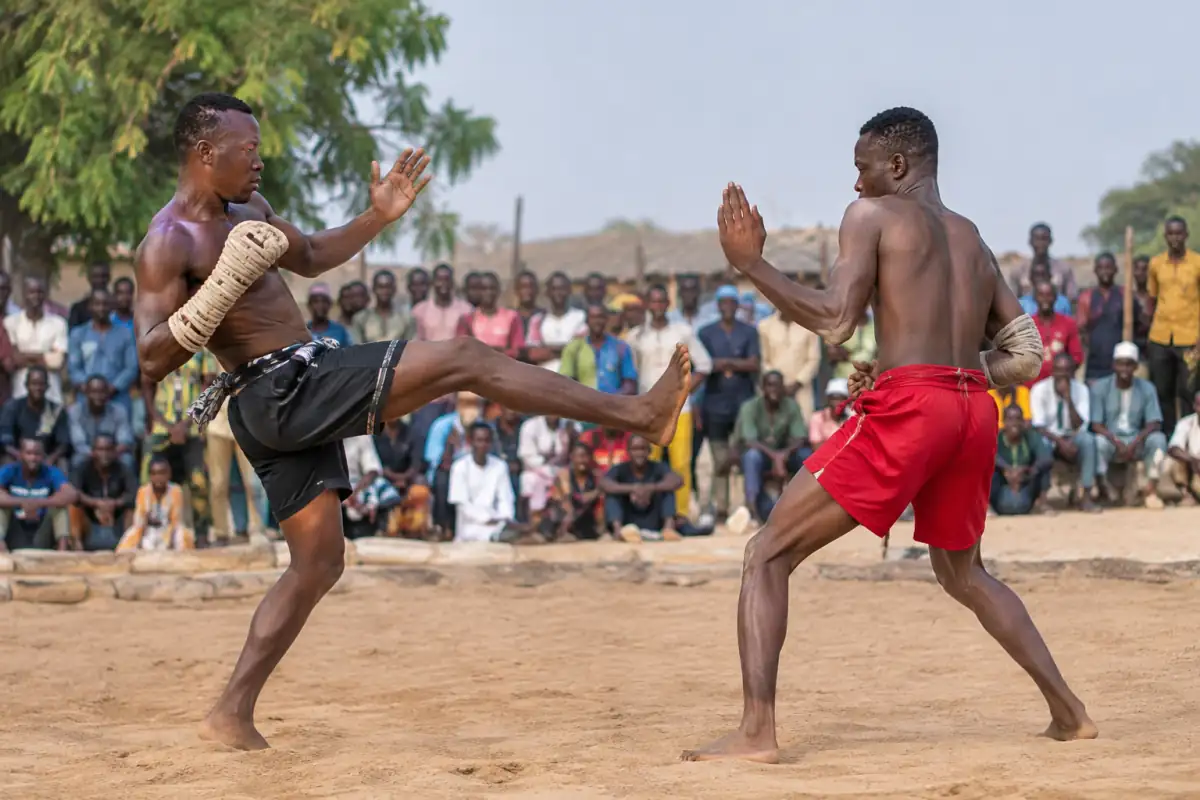 Deux combattants exécutent une garde asymétrique de dambe sur une aire de combat en plein air au Nigeria.