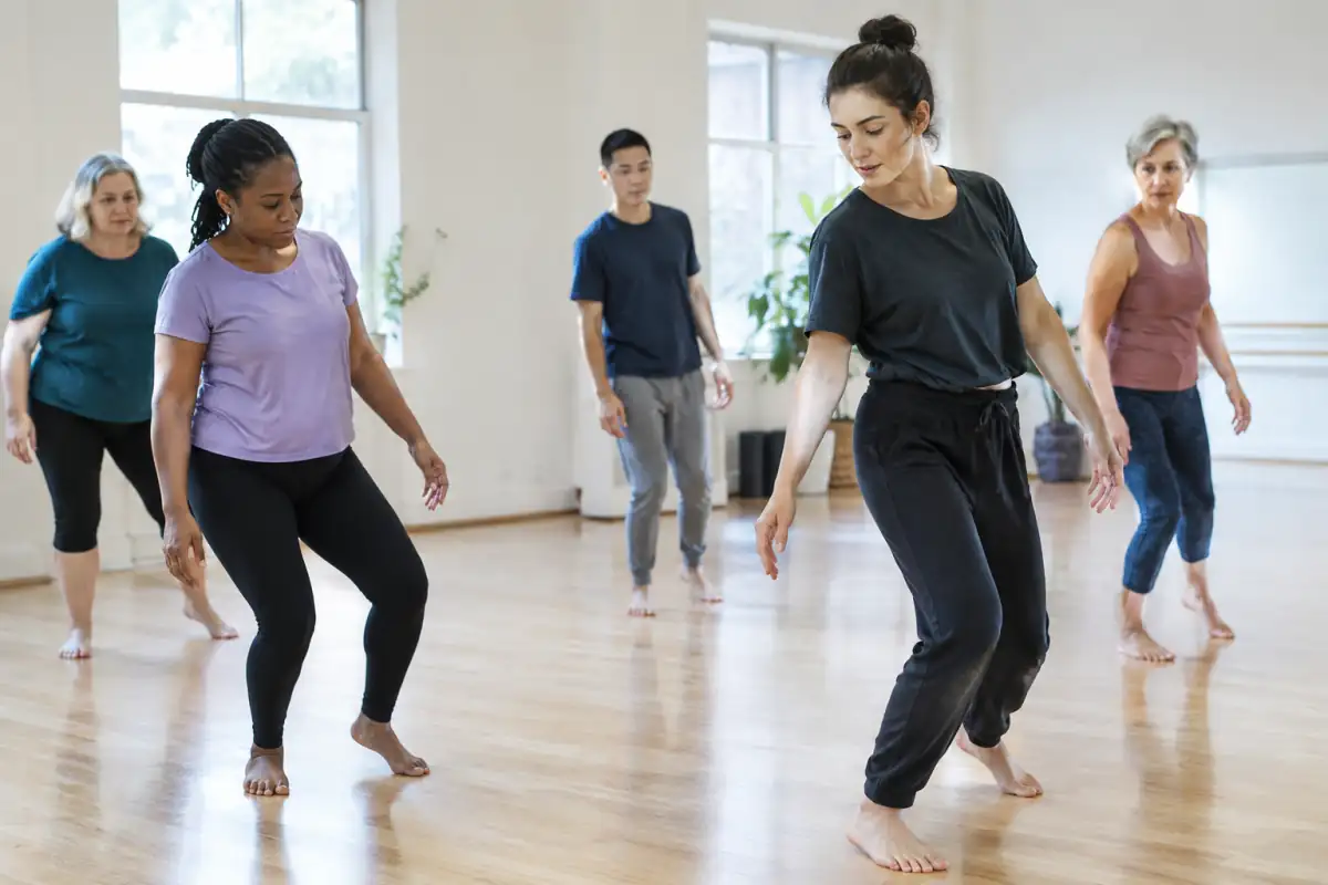 Un adulte débutant essaie un transfert de poids guidé par l’enseignant dans une salle de danse contemporaine lumineuse.