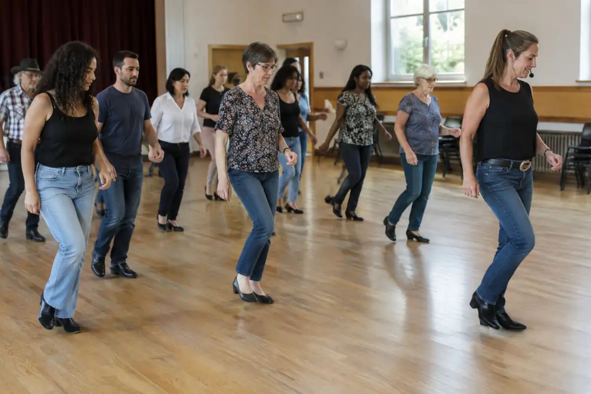 Danseurs en lignes apprenant une chorégraphie de danse country dans une salle associative, sur un parquet adapté.