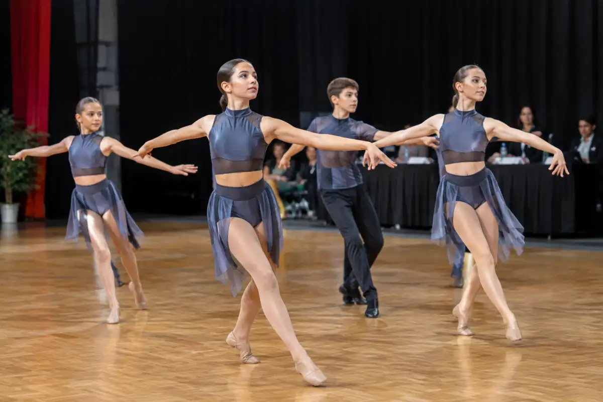 Un groupe de danseurs exécute une chorégraphie synchronisée de danse de spectacle sur une scène intérieure.