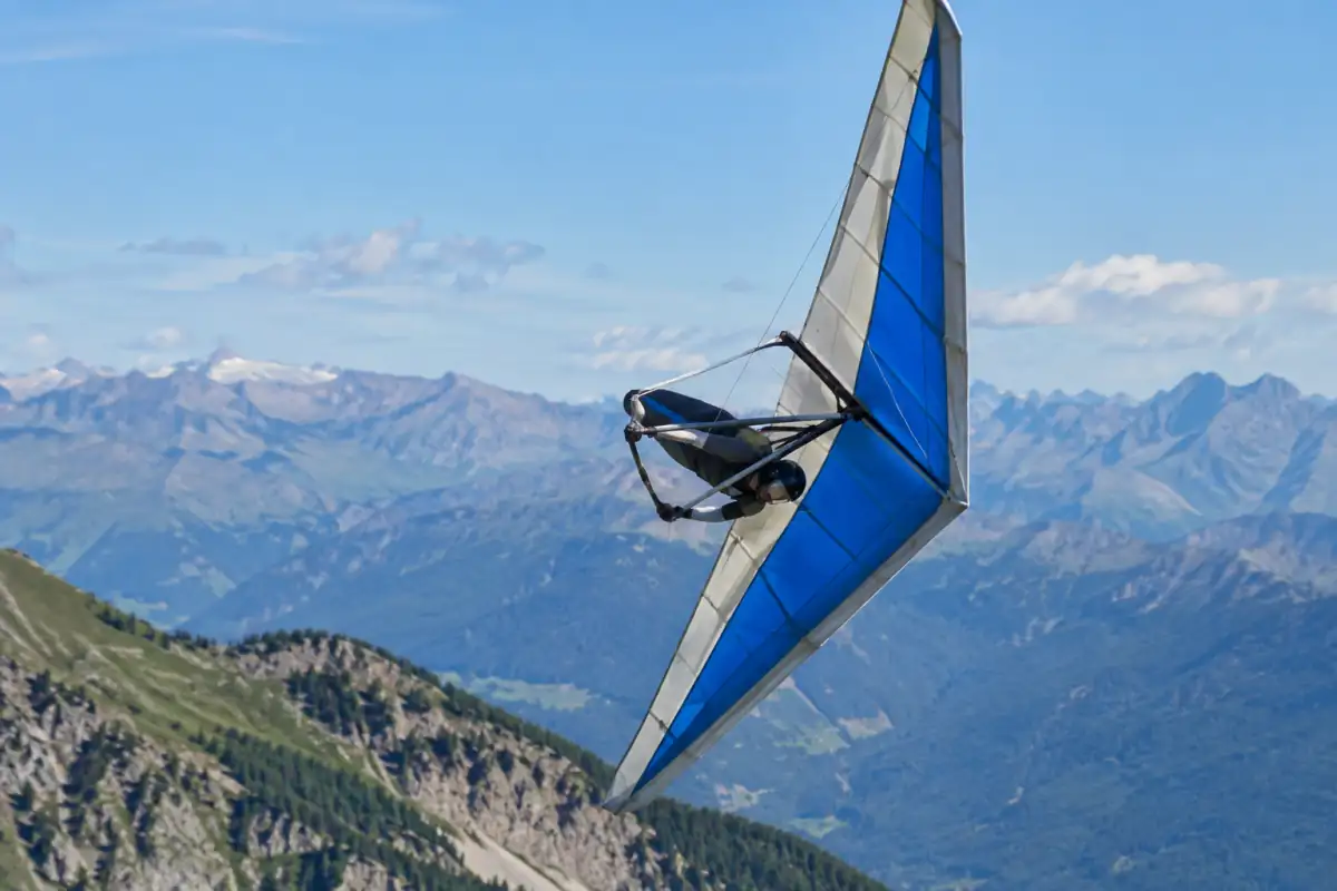 Un pilote réalise un virage fortement incliné en deltaplane acrobatique au-dessus d’un espace dégagé des Alpes françaises.