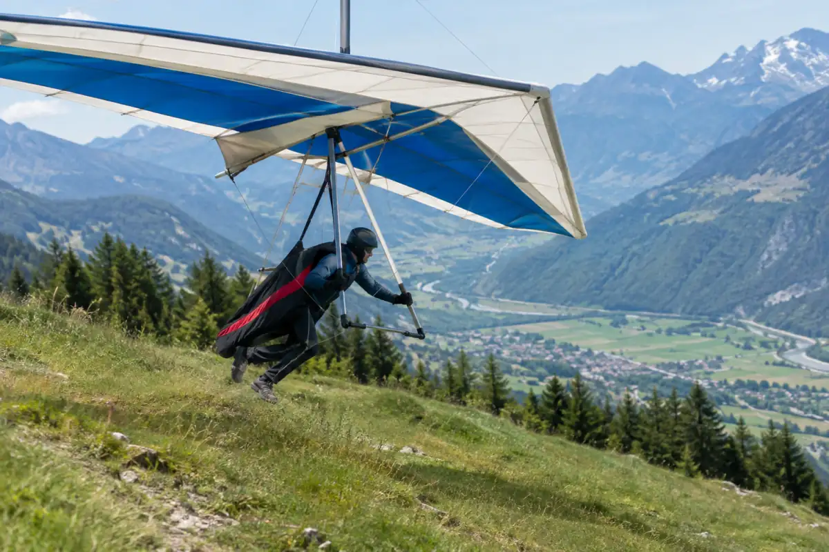 Un pilote de deltaplane s’élance à pied depuis une pente alpine sous son aile triangulaire.