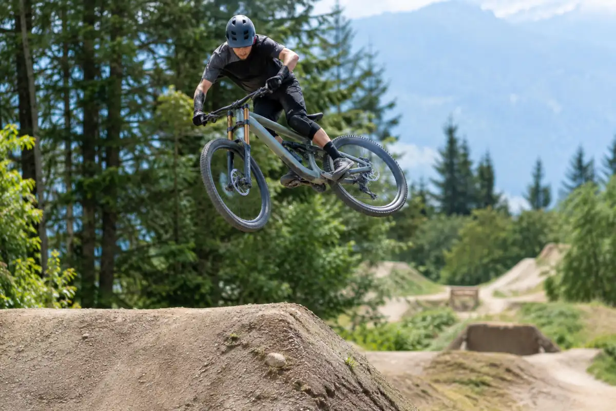 Un rider en casque réalise un saut contrôlé en VTT dirt au-dessus d’une bosse en terre dans un bike park.