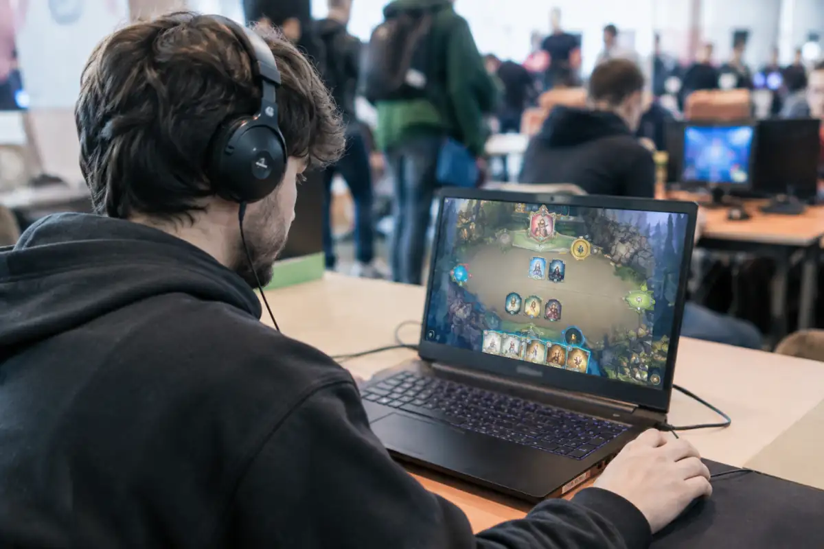 Joueur concentré sur un jeu de cartes numériques en tournoi e-sport, devant un ordinateur portable avec casque et souris.
