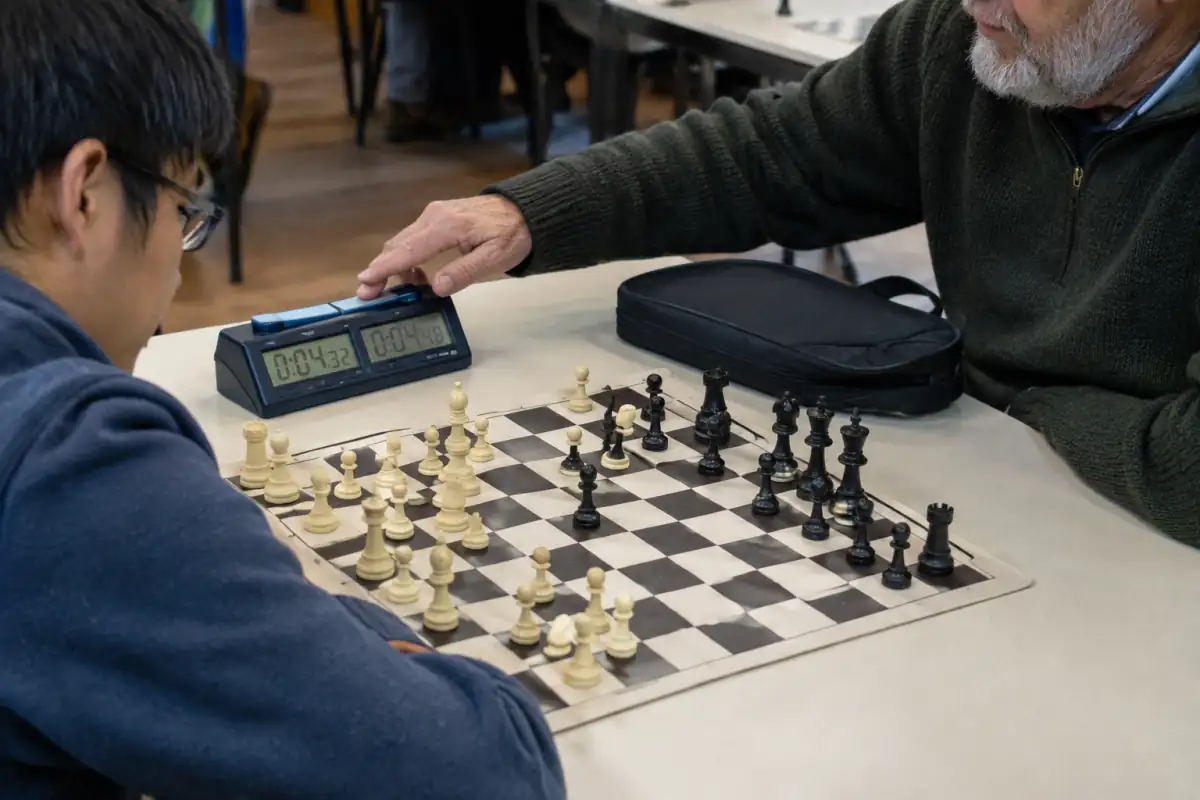 Échiquier de tournoi en vinyle, pièces Staunton lestées et pendule numérique posés sur une table de club.