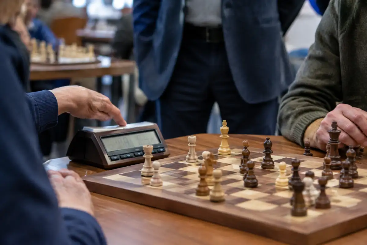 Un joueur appuie sur une pendule d’échecs après son coup, tandis qu’un arbitre surveille une partie rapide en club.