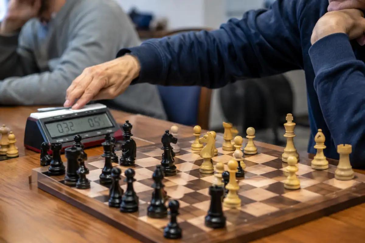 Une main déplace une pièce puis appuie sur la pendule pendant une partie d’échecs rapides au milieu de jeu.