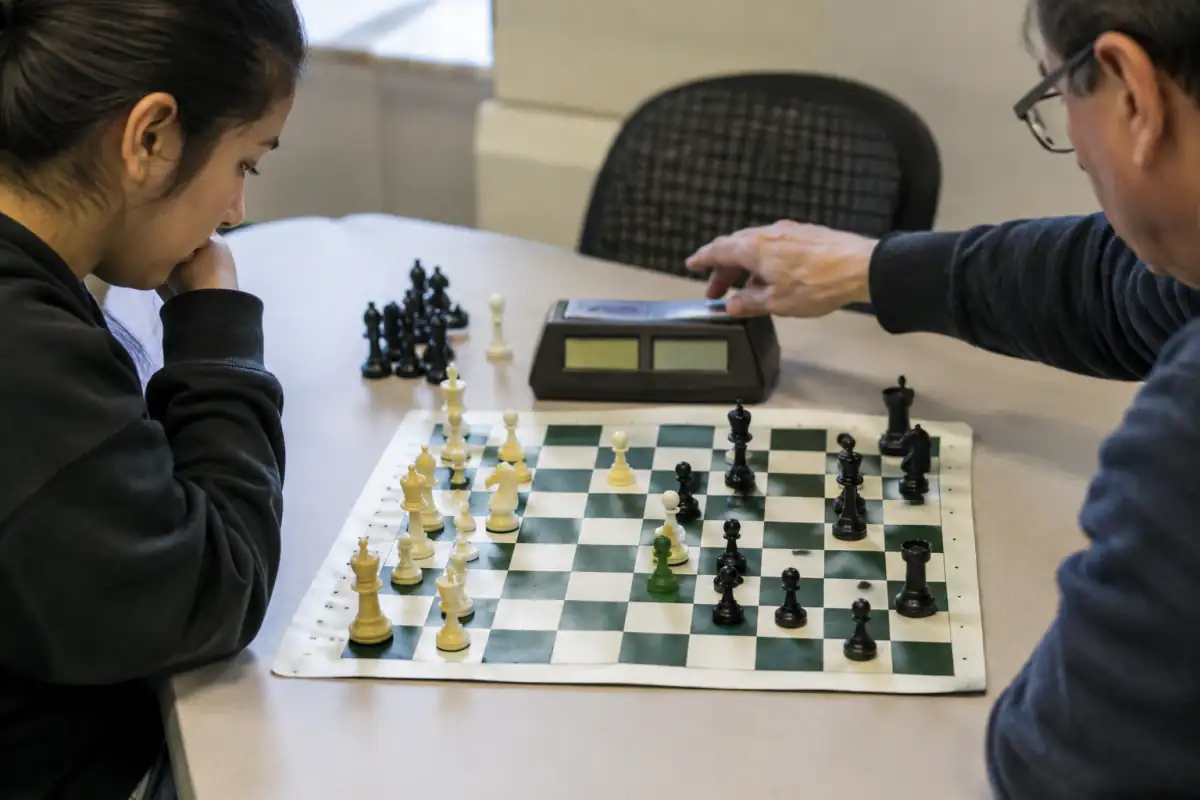 Une main presse une pendule numérique après un coup, sur un échiquier de tournoi aux pièces Staunton bien lisibles.